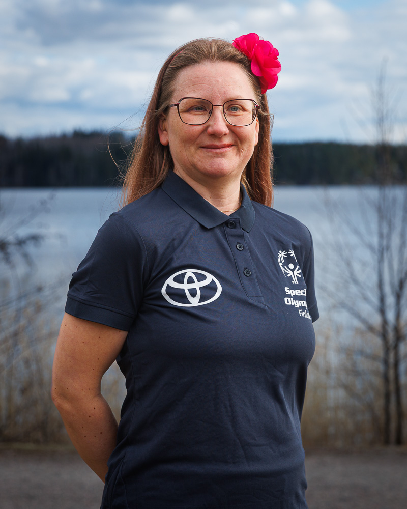 Laura Laukkanen hymyilemässä kameralle pinkki kukkakoriste hiuksissaan ja sininen SO-t-paita päällään.